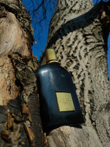 Flacon de parfum TIARA Tom Ford Black Orchid Reserve en verre noir cannelé avec plaque dorée posé sur une écorce